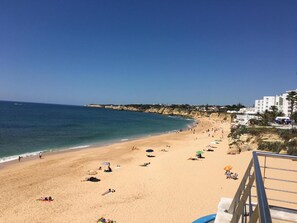 Een strand met mensen die zonnebaden, parasols en gebouwen op de achtergrond.