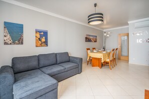 Een moderne woonkamer met een grijze hoekbank, een eettafel met stoelen en een hanglamp.