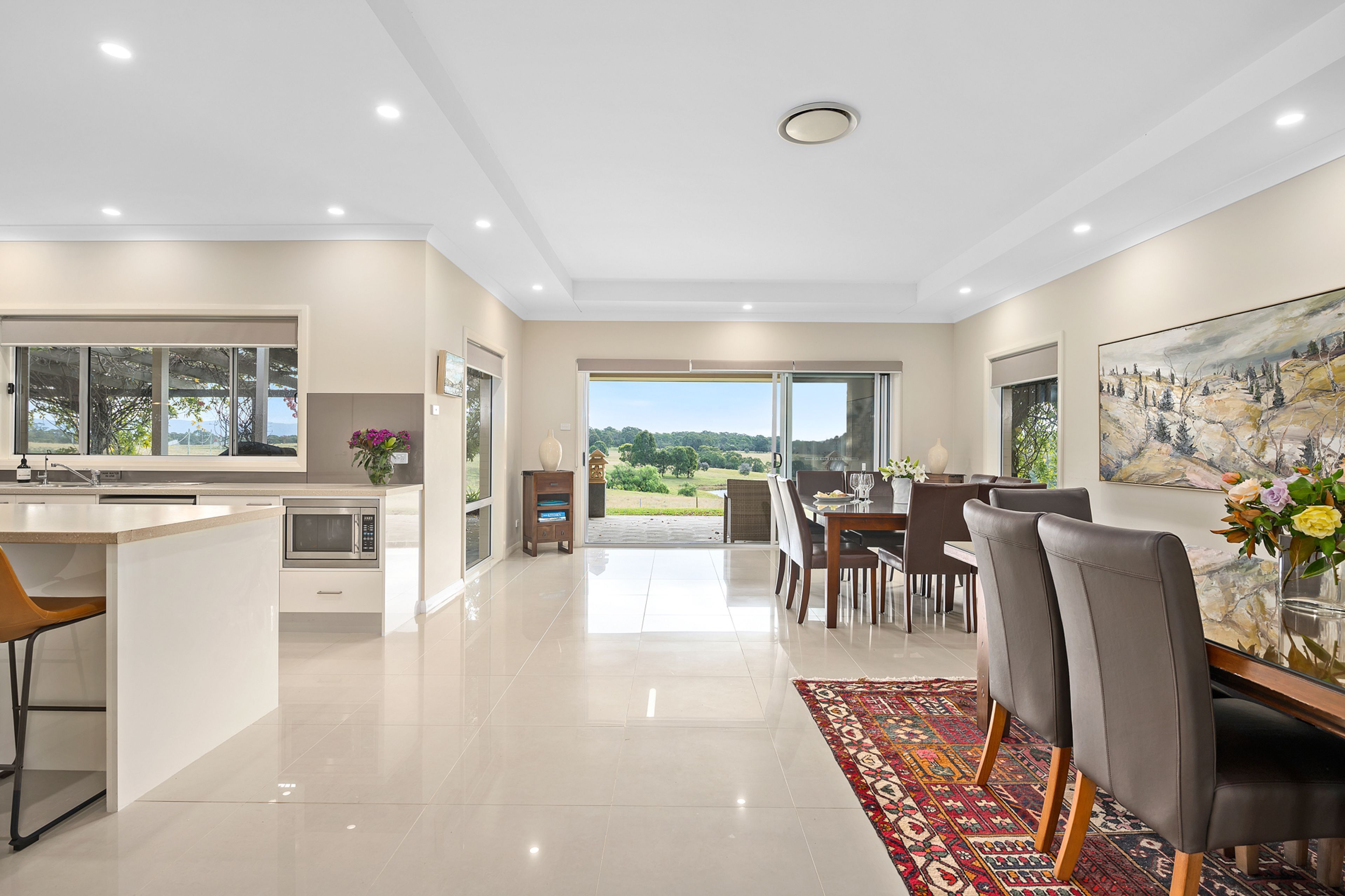 A modern kitchen with a built-in microwave, a dining area with a large table and chairs, and a view of the outdoors through a glass door.