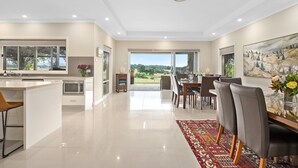 A modern kitchen with a built-in microwave, a dining area with a large table and chairs, and a view of the outdoors through a glass door. - Mole Hill Farmhouse (Keinbah)