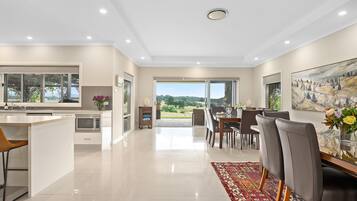 A modern kitchen with a built-in microwave, a dining area with a large table and chairs, and a view of the outdoors through a glass door.
