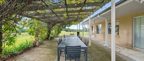 Une terrasse extérieure avec une table et des chaises, entourée d’une pergola en bois et de verdure.