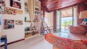 A room with a patterned sofa, a chair, a ceiling fan, a window with curtains, and a wall with various framed photos. - Villa 'Anna Maria' with Sea View, Private Terrace and Wi-Fi (Vulcano)