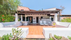 A covered outdoor patio with a dining area, a kitchen, and a seating area with white walls and terracotta flooring. - Villa 'Anna Maria' with Sea View, Private Terrace and Wi-Fi (Vulcano)