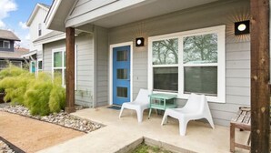 Ein Wohnhaus mit überdachter Veranda, einer blauen Tür und einem kleinen Tisch mit Stühlen.