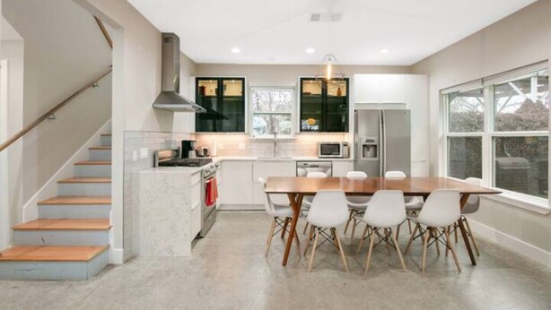Eine moderne Küche mit Essbereich, ausgestattet mit einem Holztisch und Stühlen, einem eingebauten Backofen und einem großen Fenster für natürliches Licht.
