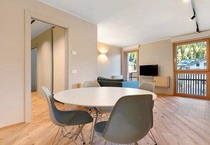 A modern room with a round table, chairs, a sofa, a TV, and a window with a view.