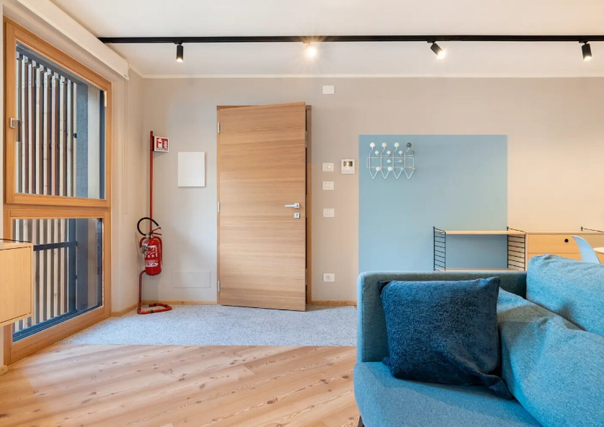 Una habitación moderna con suelo de madera, un sofá azul, una puerta de madera y un extintor.