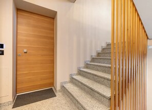 Una puerta de madera, un recibidor con alfombra y una escalera con barandilla de madera.