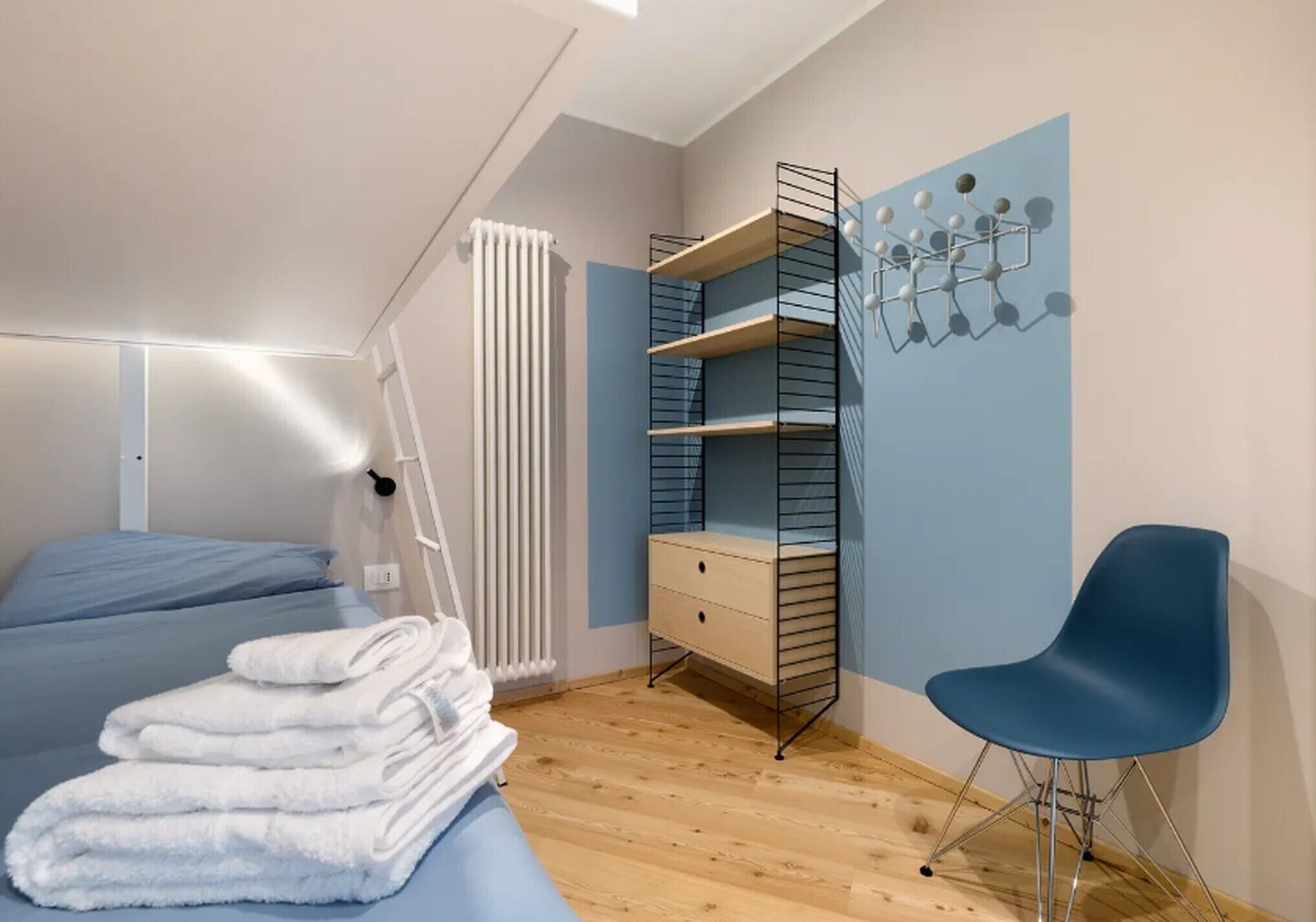 Une chambre à coucher comprenant un lit, une chaise, un radiateur et une étagère fixée au mur.