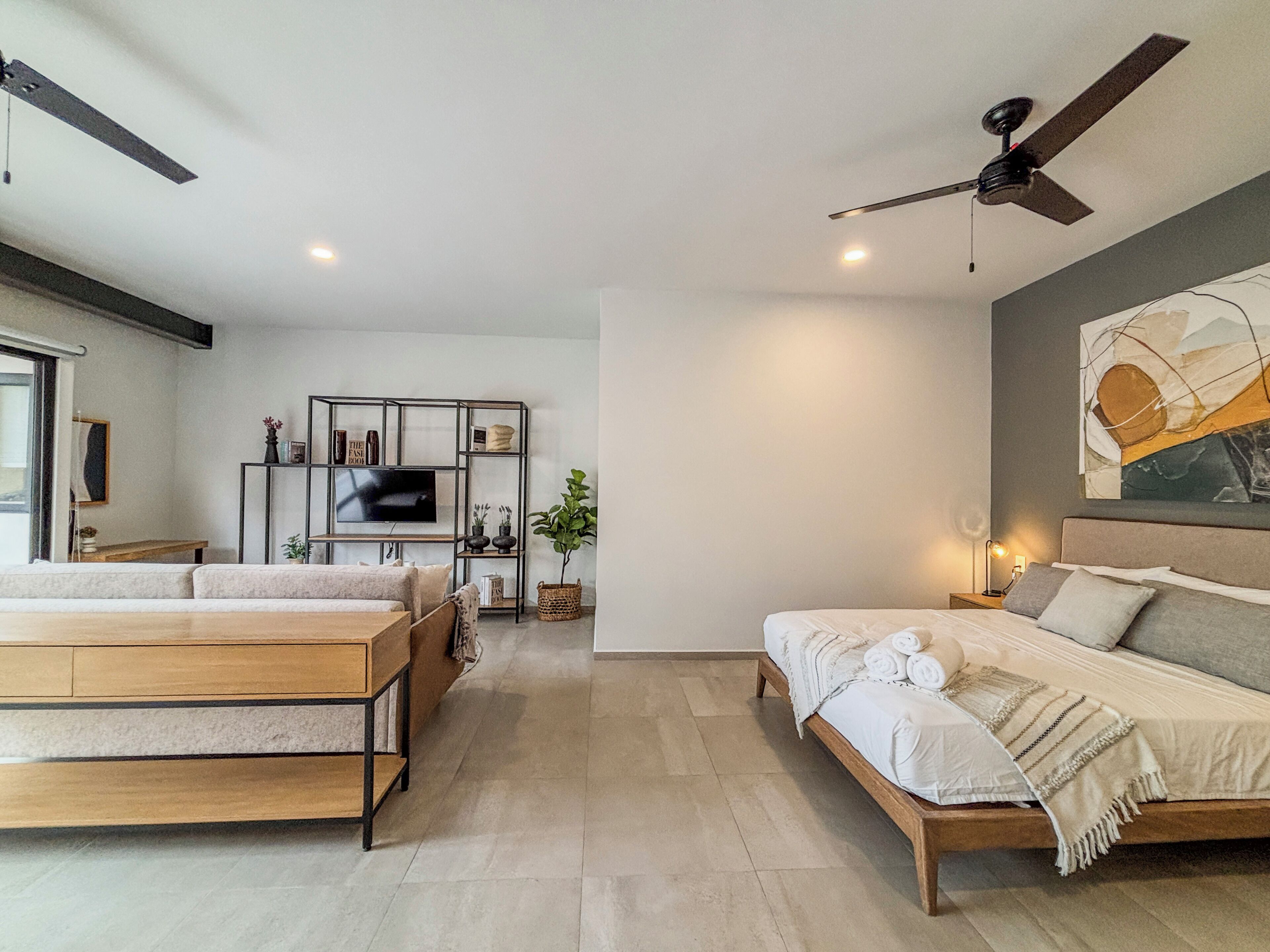 A modern bedroom with a bed, a sofa, a TV, and a ceiling fan.