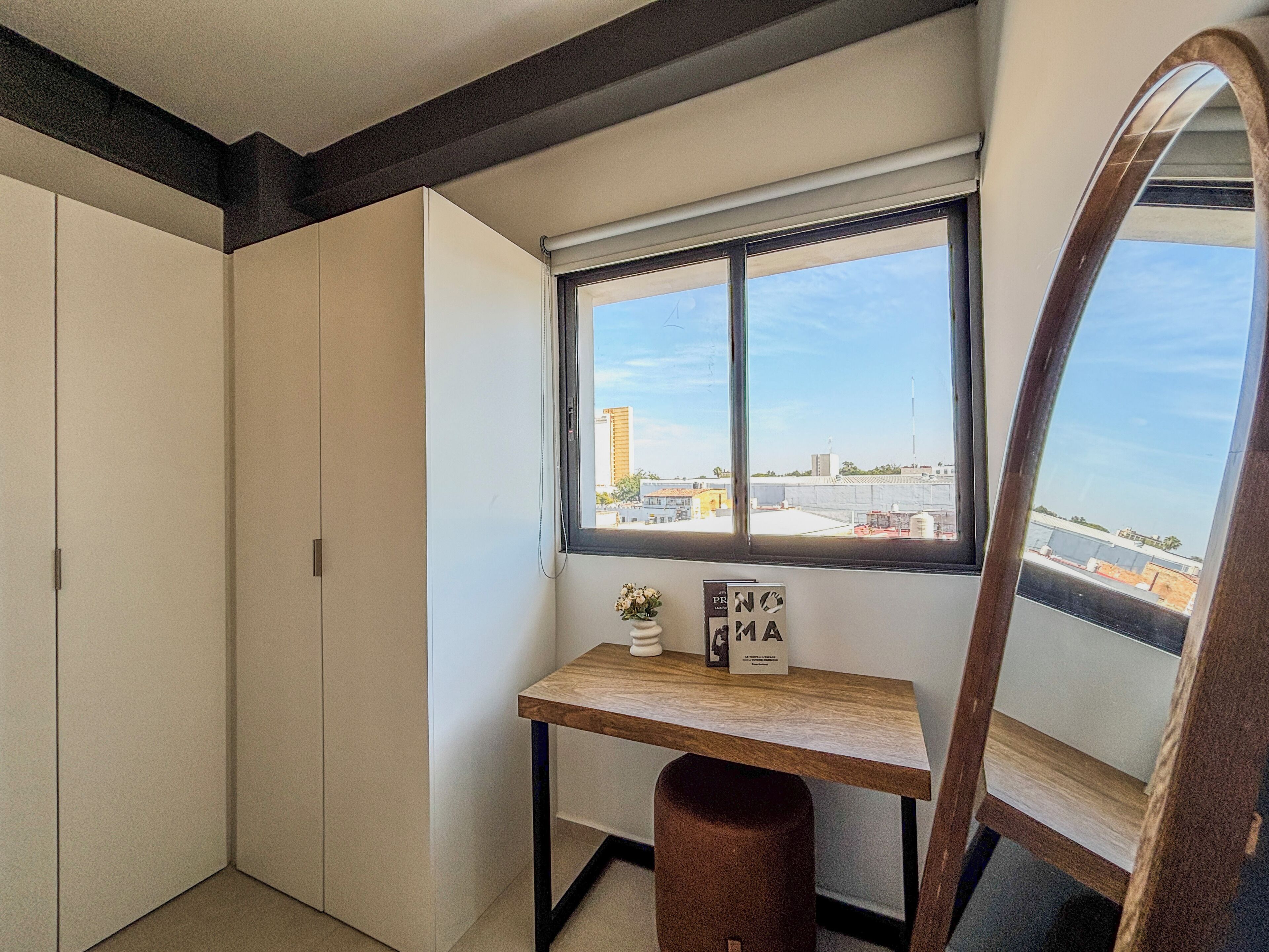 Ein kleines Zimmer mit Schreibtisch, Spiegel und Fenster.