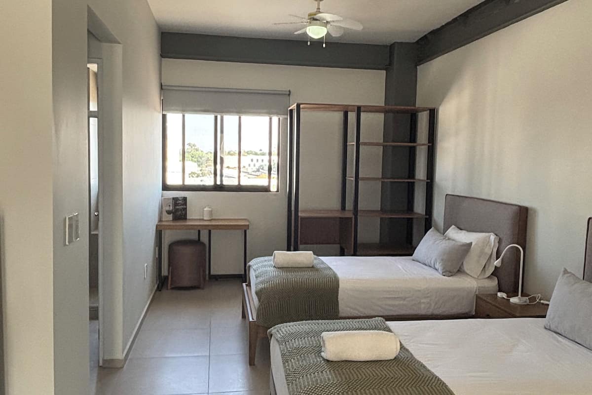 A hotel room with two beds, a desk, and a window.