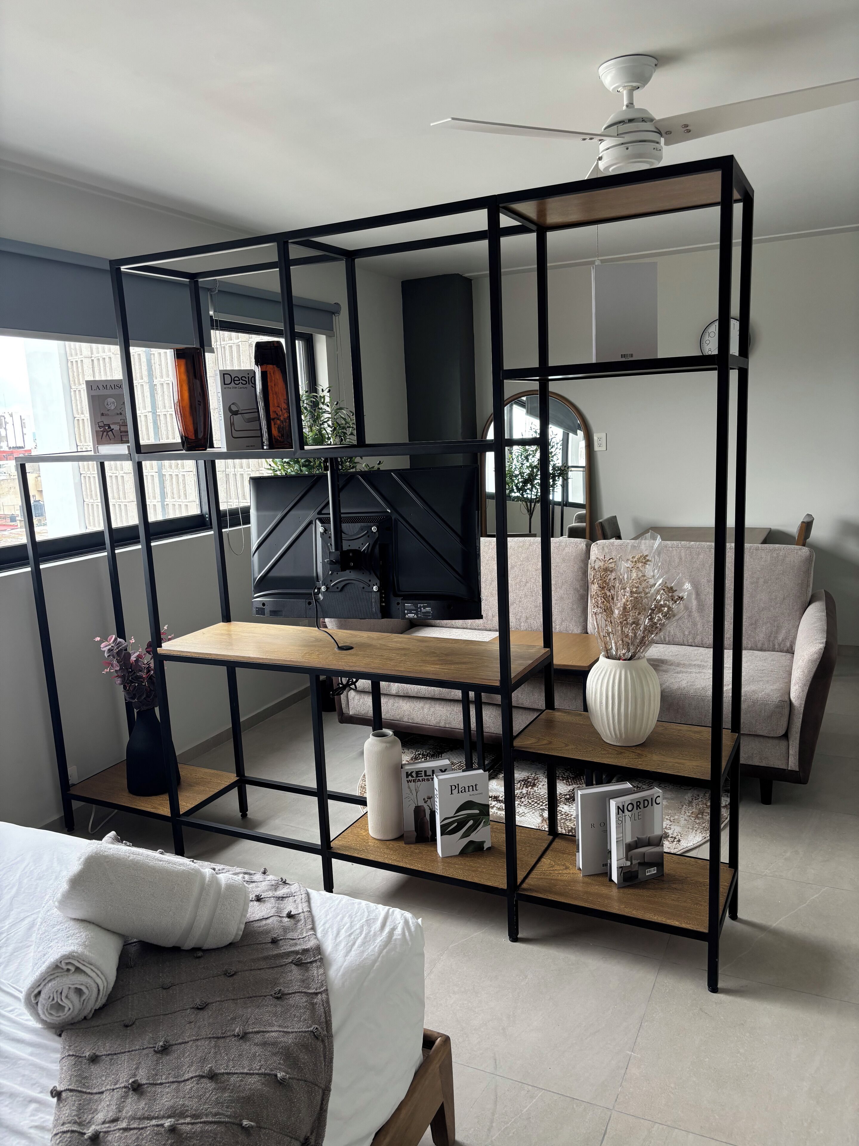 Un salon moderne avec une étagère en métal noir, une table basse en bois, un canapé et un téléviseur.
