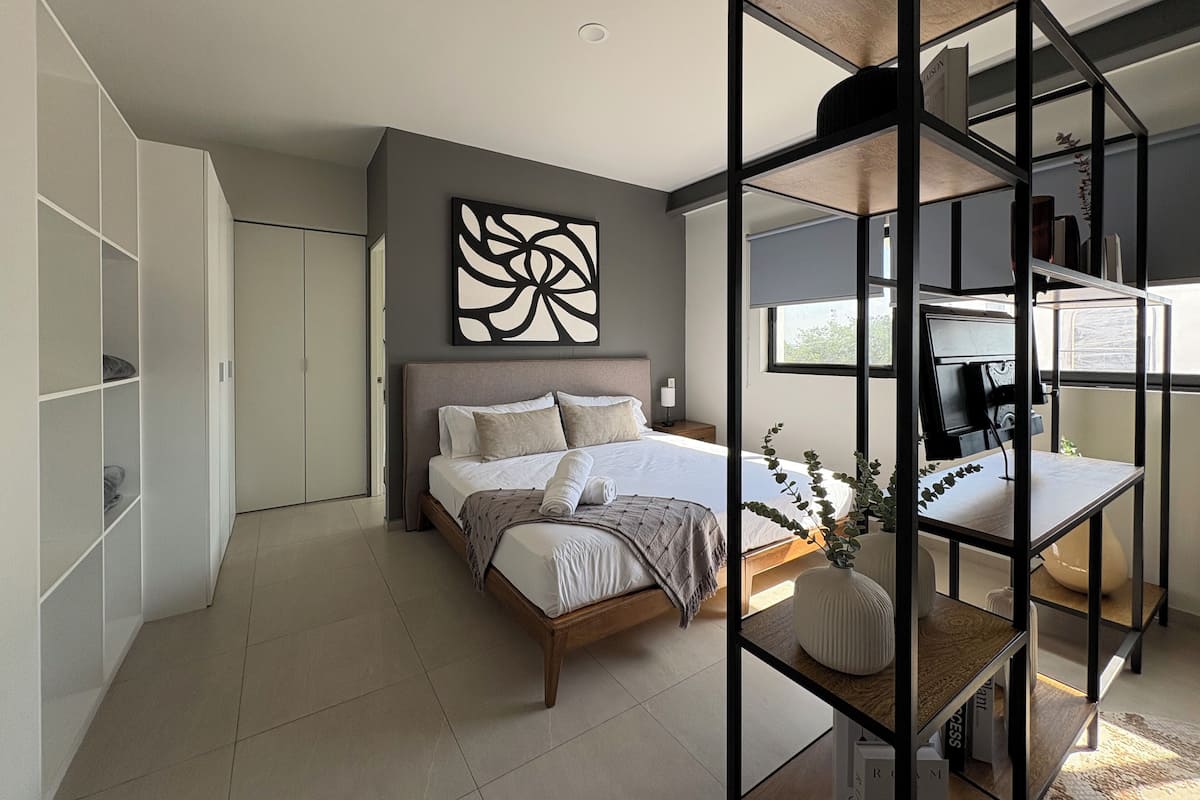 A modern bedroom with a bed, a desk, and a shelving unit.