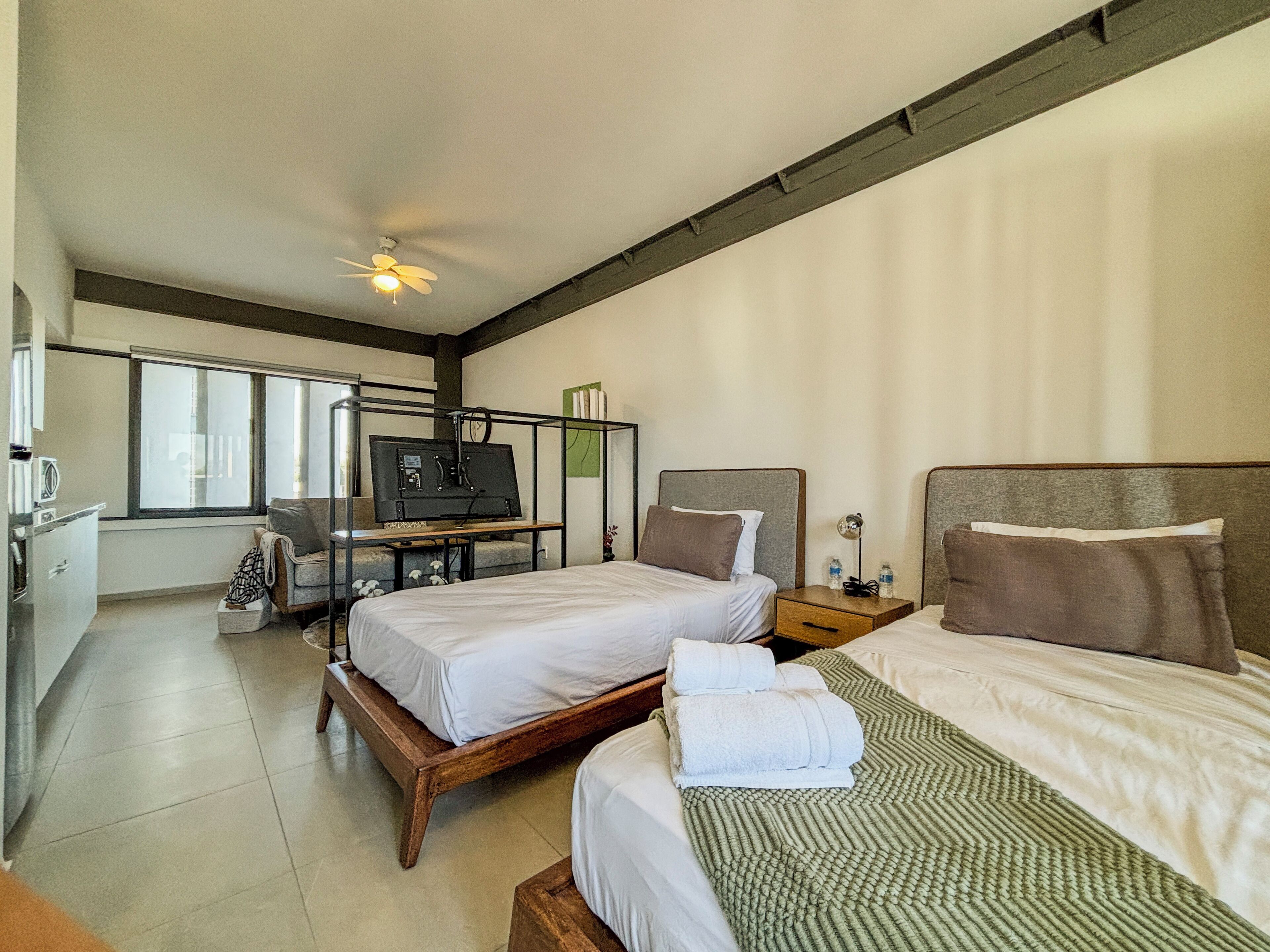 A hotel room with two beds, a TV, a desk, and a window.