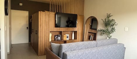 A modern living room with a grey sofa, wooden paneling, a ceiling fan, a flat-screen TV, and a potted plant.