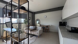 Ein modernes Wohnzimmer mit einer Couch, einem Couchtisch und einem Essbereich mit Stühlen. Es gibt eine Küchenzeile mit Spüle und Herd.