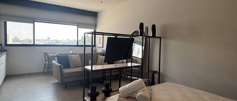 Un dormitorio moderno con cama, escritorio y silla. Hay una ventana que proporciona luz natural y vistas al exterior.