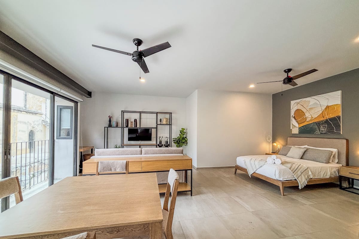A modern living room with a dining area, a sofa, a TV, and two ceiling fans.