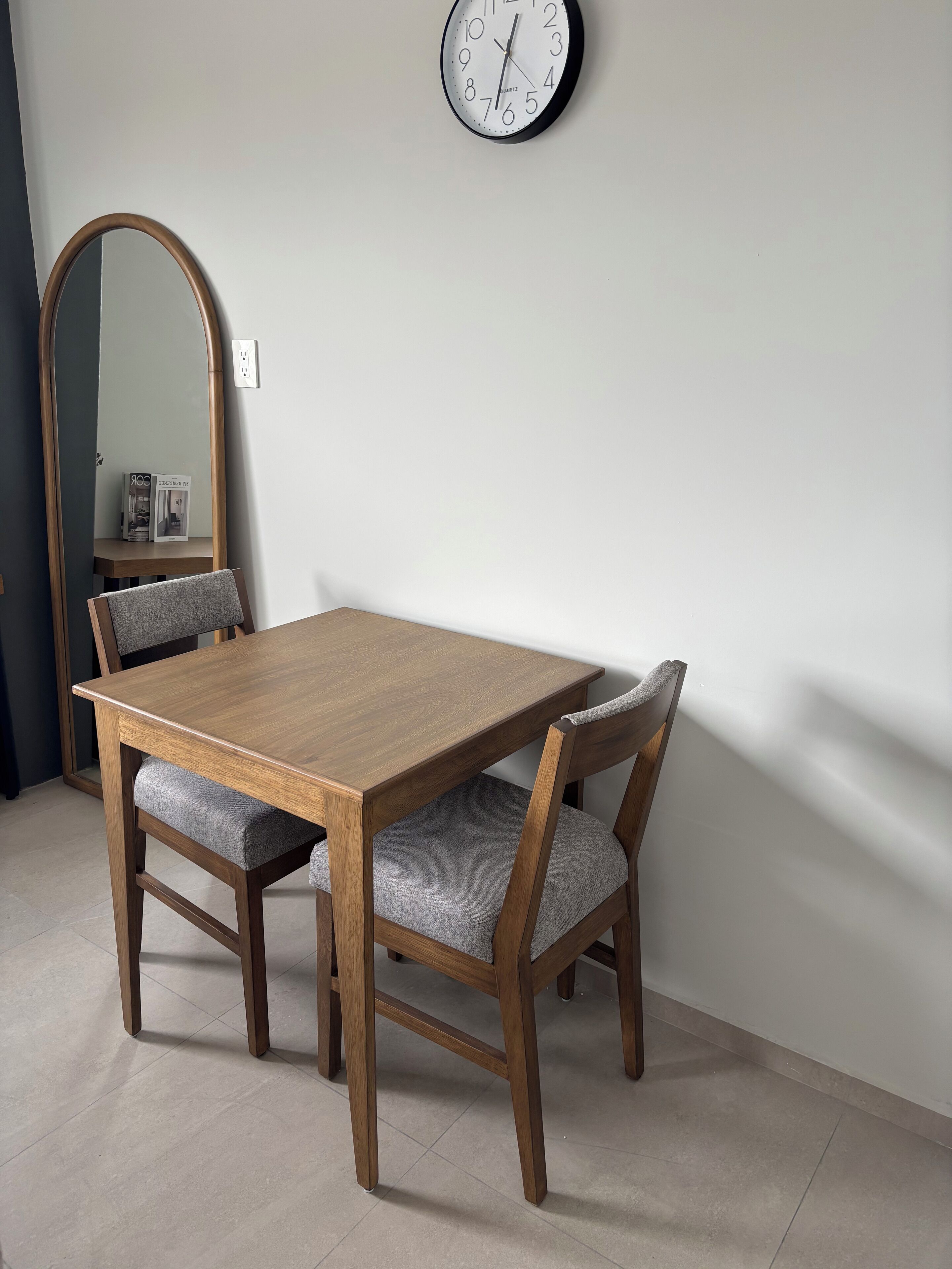 A dining table with two chairs, a wall clock, and a mirror.