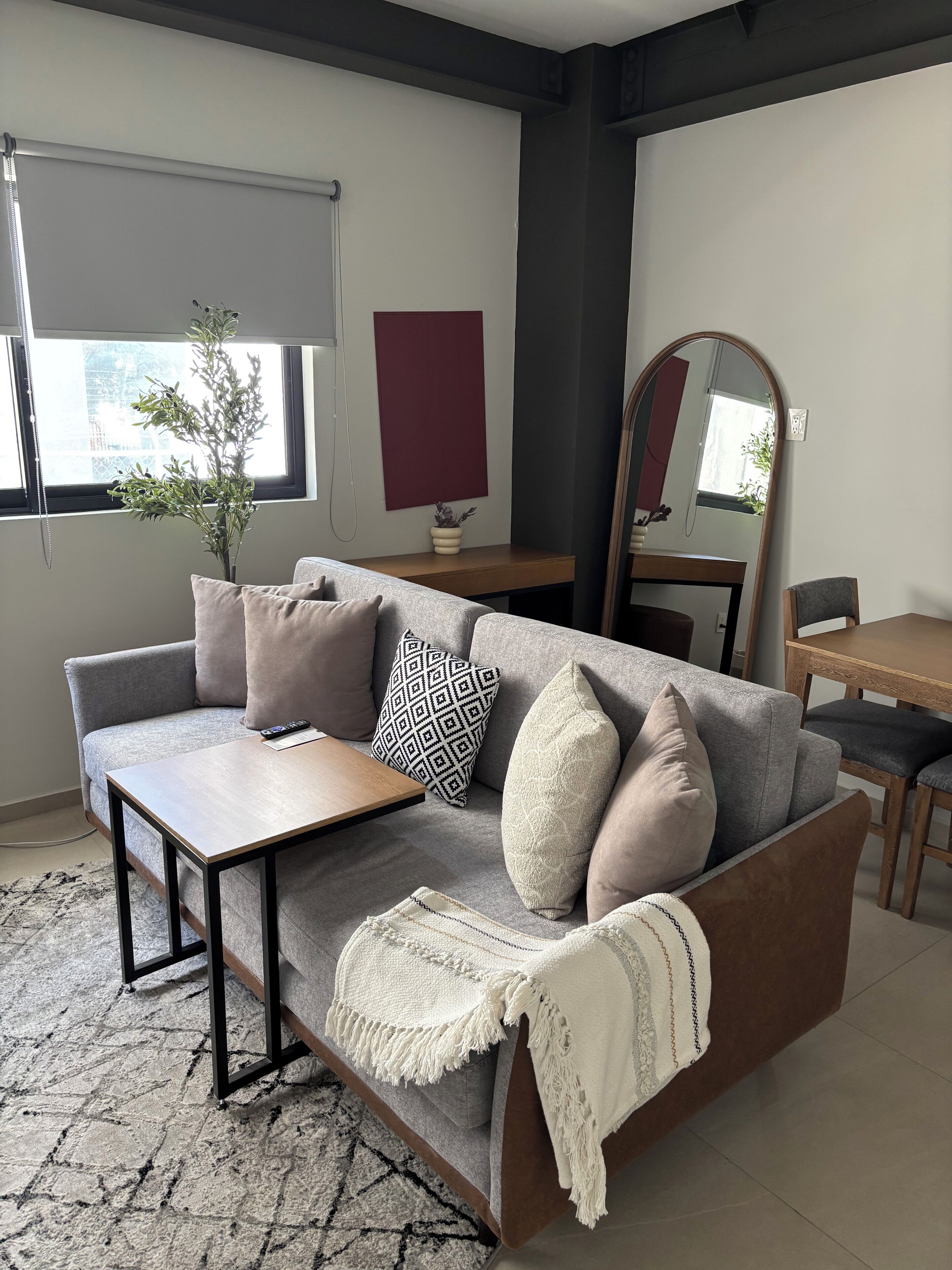 Een moderne woonkamer met een grijze bank, een houten salontafel, een gebreid plaid en een plant in een pot.