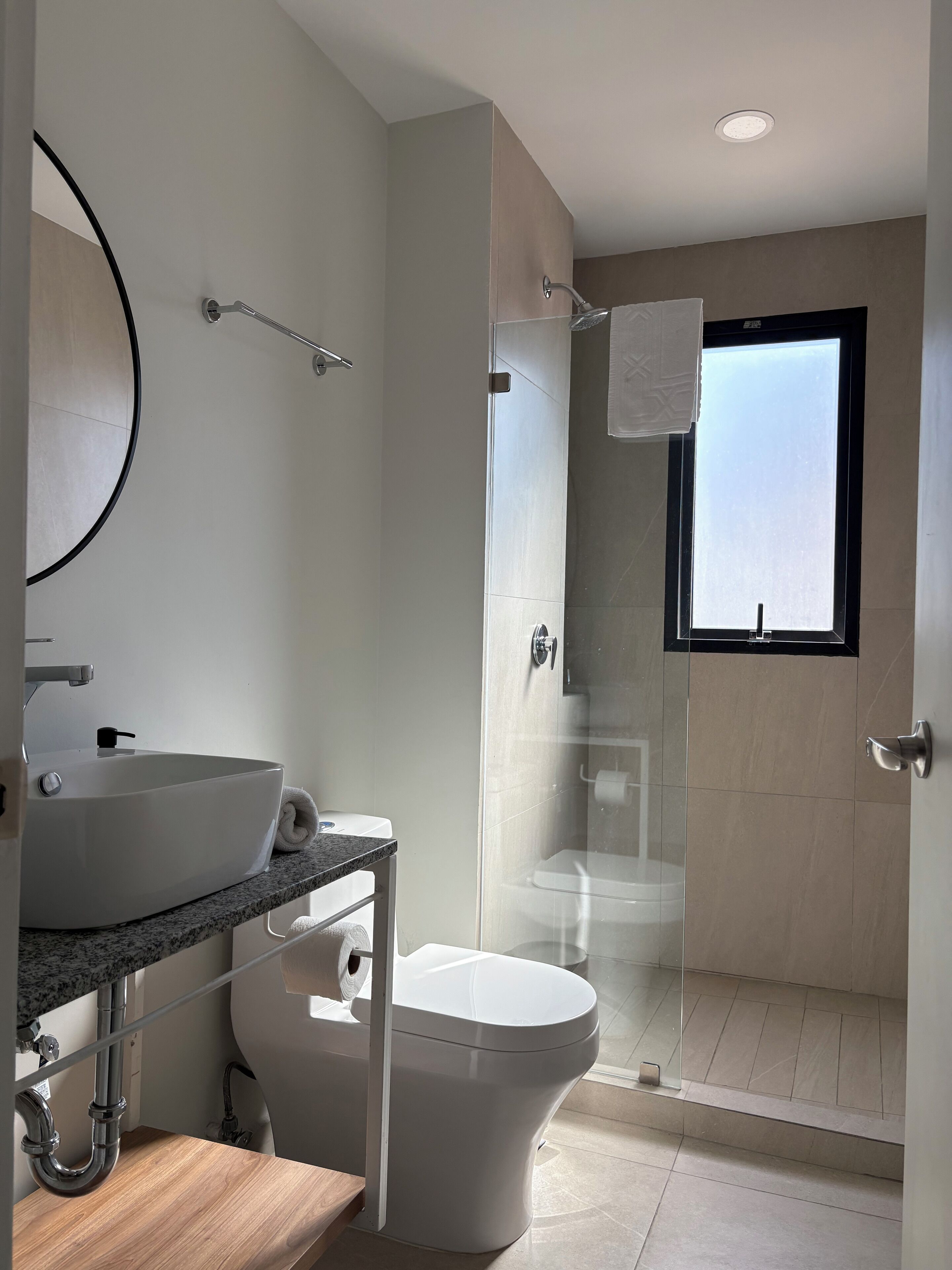 Un baño moderno con un lavamanos blanco, ducha con mampara de vidrio y un inodoro.