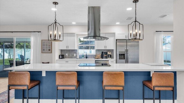 Una cucina moderna con un'isola ampia, sgabelli da bar, elettrodomestici in acciaio inossidabile e illuminazione a sospensione.