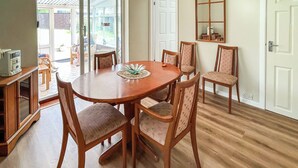 A dining area with a wooden table and six chairs, a television on a cabinet, and a large window with a view of the outside. - 3 bedroom accommodation in Weymouth (Weymouth)