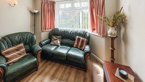 A room with a green leather sofa, a wooden coffee table, and a floor lamp. - 3 bedroom accommodation in Weymouth (Weymouth)