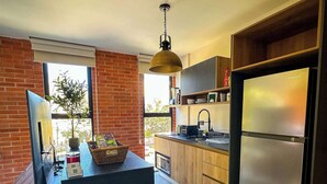A modern kitchen with a central island, wooden cabinets, a stainless steel refrigerator, and a hanging pendant light. - Americana apartment with rooftop pool (Guadalajara)