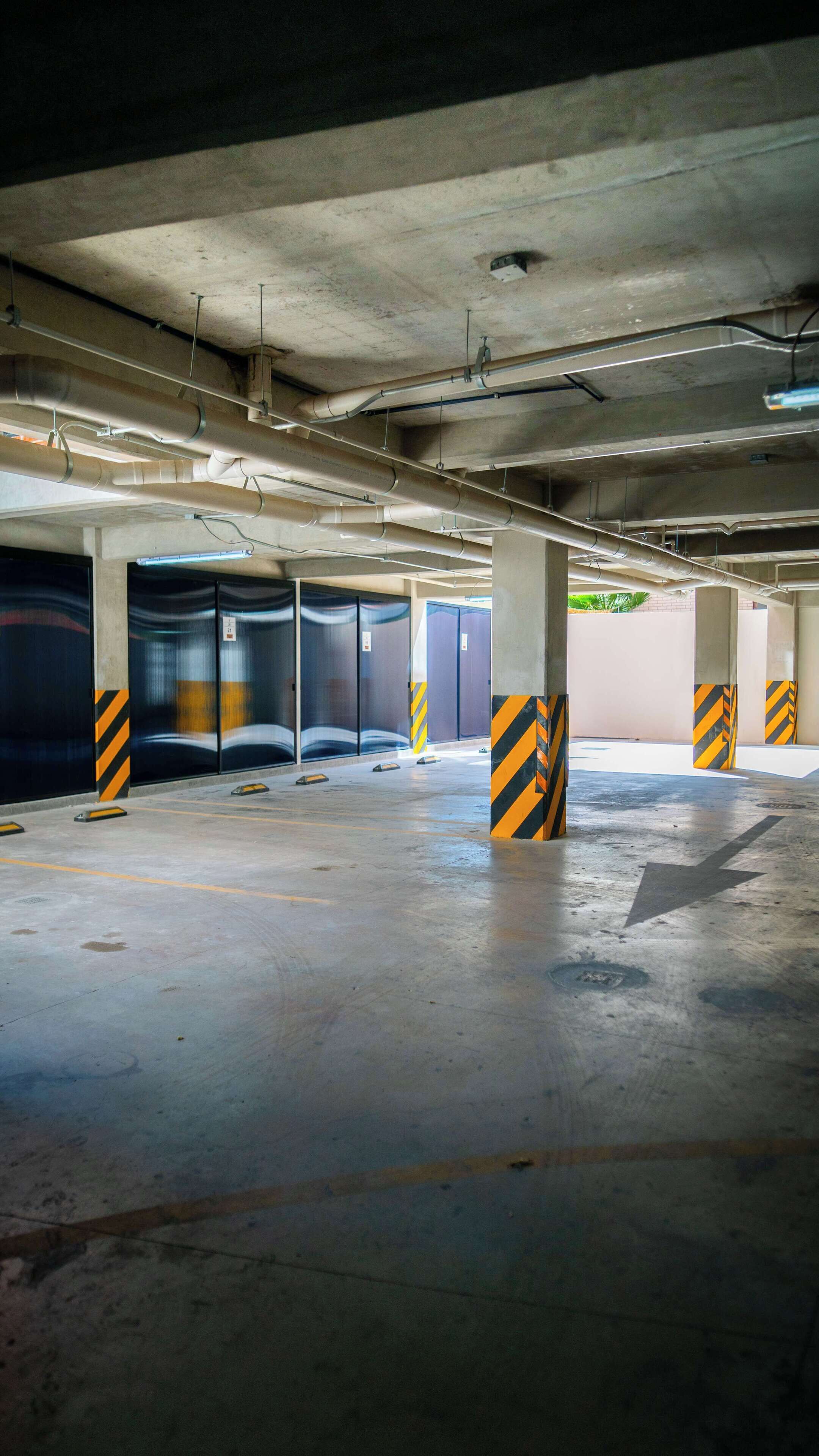 Garagem subterrânea com pilares de concreto, iluminação fluorescente e chão limpo e vazio.