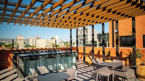 A rooftop terrace with a pergola, outdoor seating, and a city view.