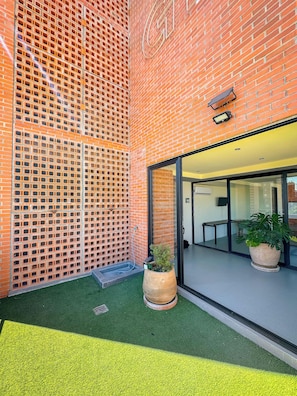 A brick building with a glass door entrance, a small outdoor seating area with a table and chairs, and a potted plant.