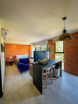A modern kitchen with a central island, a dining area with stools, a blue sofa, and a brick wall. - Americana apartment with rooftop pool (Guadalajara)