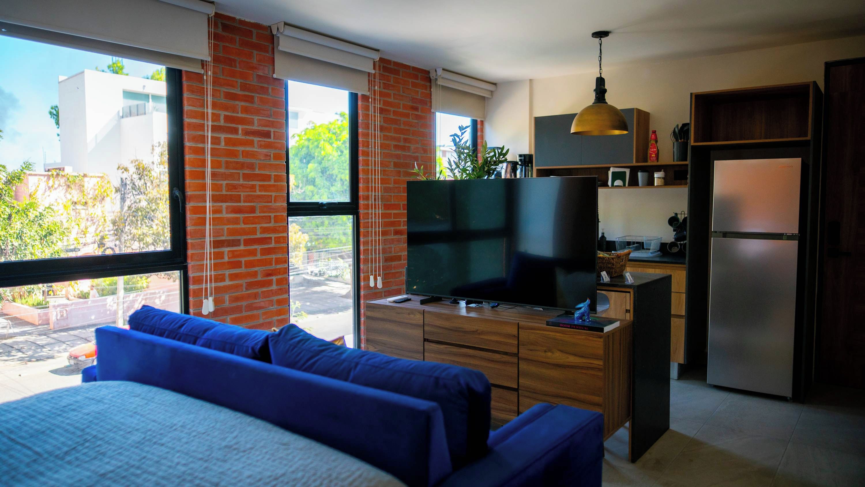 Ein moderner Wohnraum mit großem Fenster, Flachbildfernseher, einer Couch, einer Küchenzeile und einem Kühlschrank.