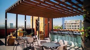 A rooftop terrace with outdoor seating, potted plants, and a view of the cityscape.