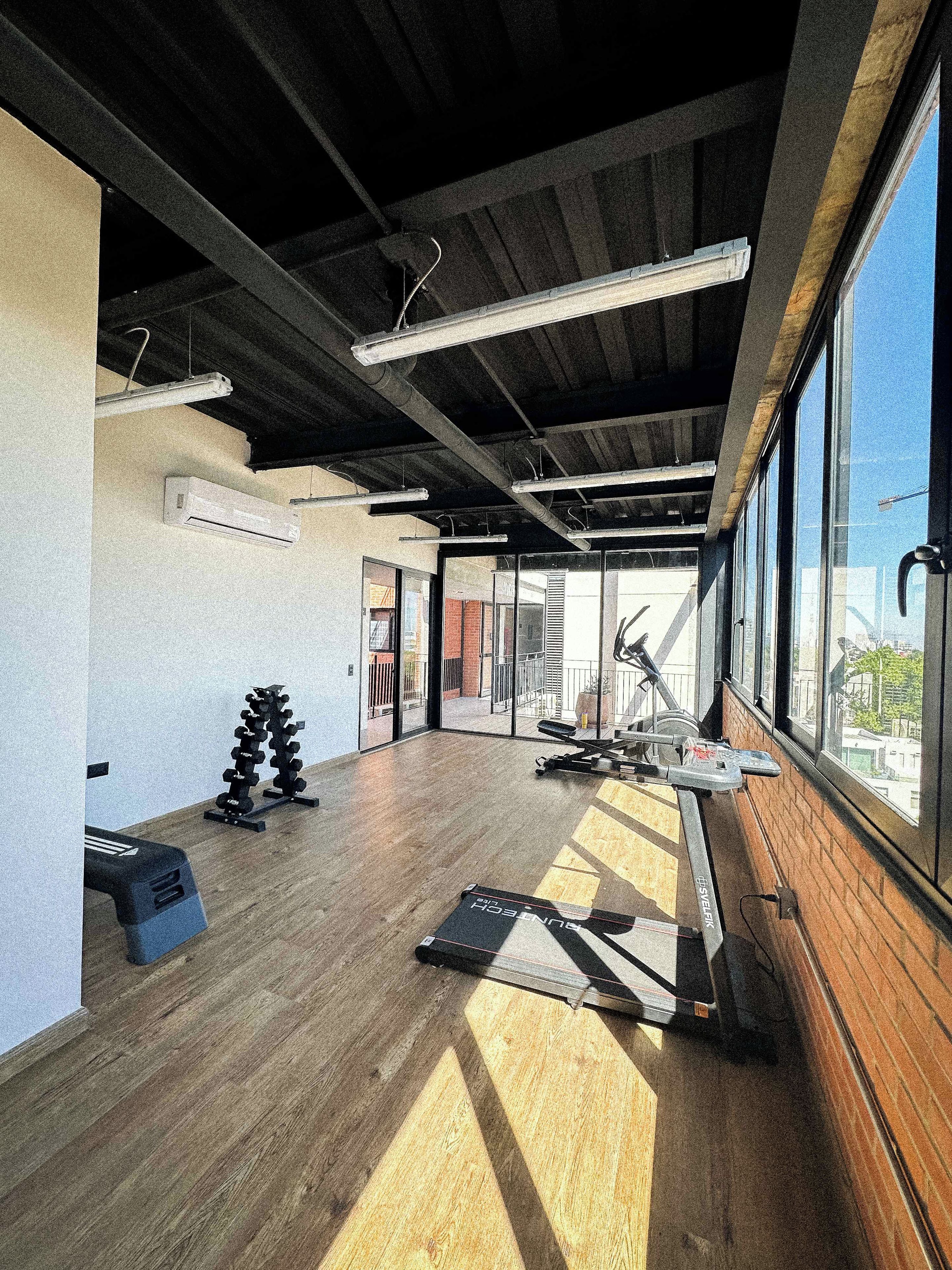 A spacious gym with exercise equipment, large windows, and a high ceiling.
