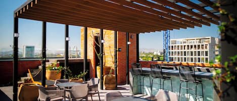 Une terrasse sur le toit, aménagée avec des espaces de détente en plein air, des plantes en pot et offrant une vue sur le paysage urbain.
