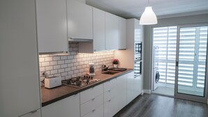 A modern kitchen with white cabinets, a gas stove, a sink, and a built-in oven. - São Pedro Apartment (Vila Franca Do Campo)
