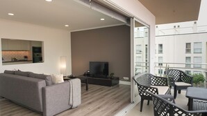 A modern living room with a sofa, coffee table, TV, and balcony with outdoor furniture. - São Pedro Apartment (Vila Franca Do Campo)
