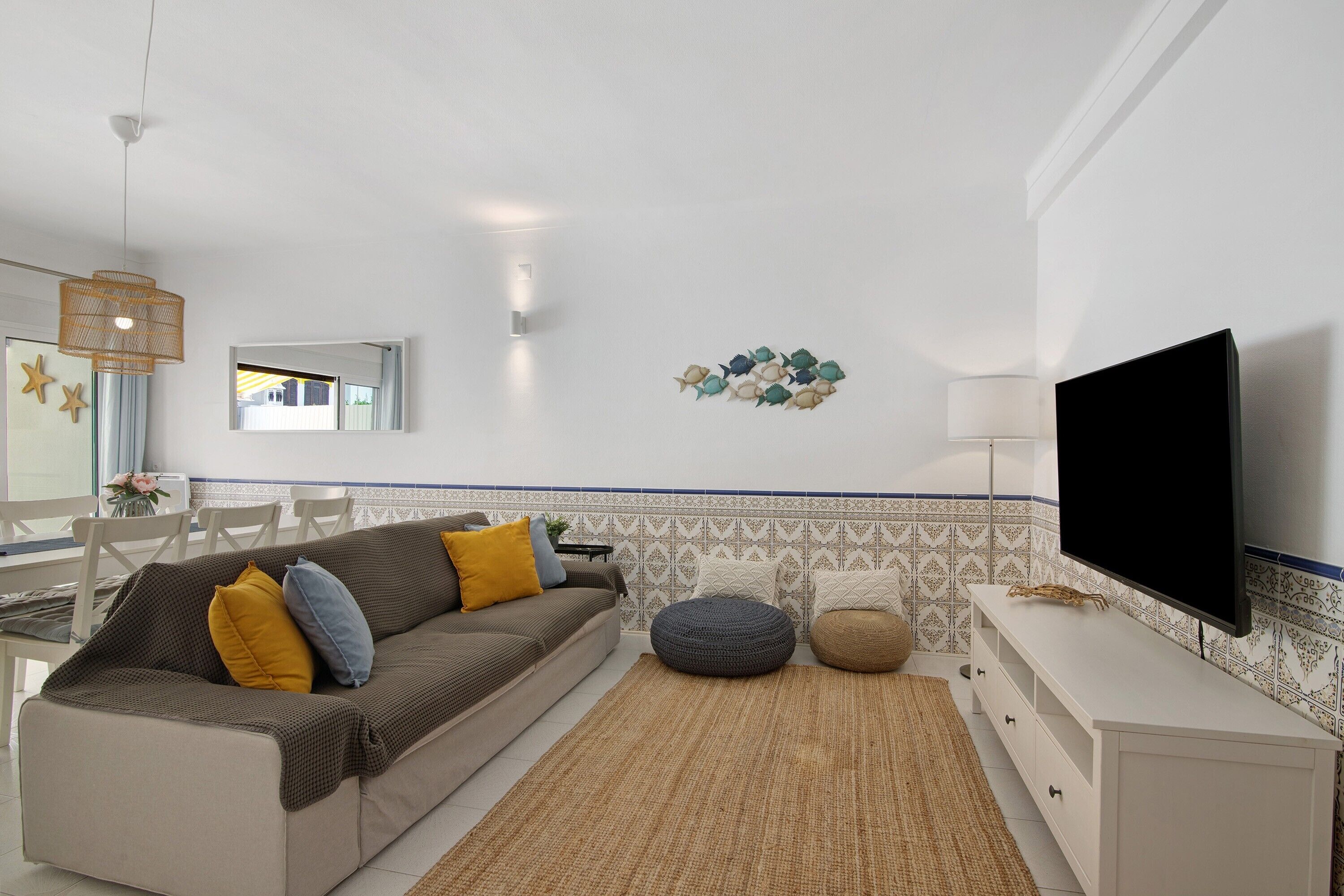 Een woonkamer met een bank, voetenbankje, flatscreen-tv en een behang met patroon.