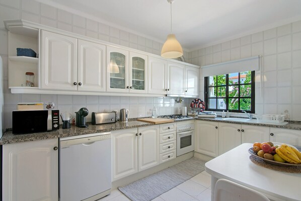 A kitchen with white cabinetry, a granite countertop, a coffee maker, a toaster, and a fruit bowl.