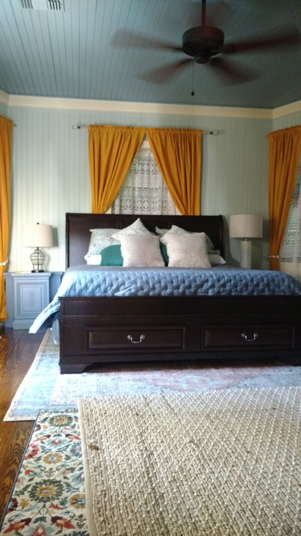 Une chambre avec un grand lit, deux tables de chevet, un ventilateur de plafond et un tapis à motifs.