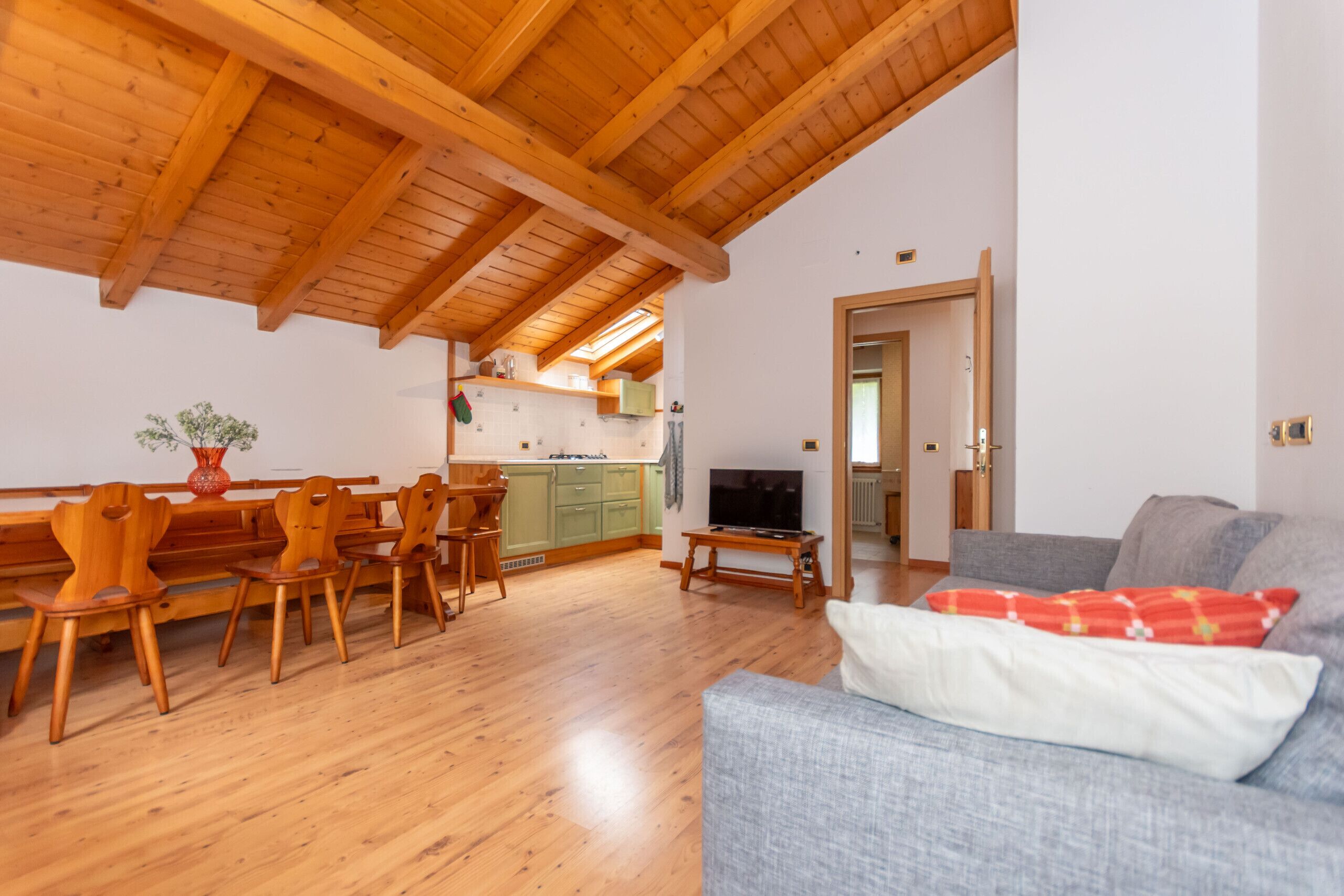 Amplia sala de estar con piso de madera, un comedor, un sofá gris y una cocina al fondo.