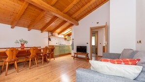 A spacious living area with wooden flooring, a dining set, a grey sofa, and a kitchen in the background. - La Casa di Elvira-Mansarda (Alleghe)