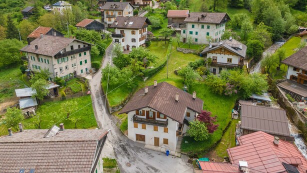 A cluster of traditional European-style buildings with sloped roofs, surrounded by lush greenery and a narrow road. - La Casa di Elvira-Mansarda (Alleghe)