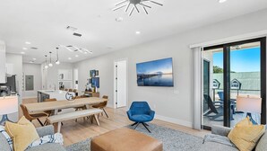 A modern living room with a dining area, a large TV mounted on the wall, and a sliding glass door leading to an outdoor patio.