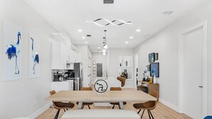 A modern kitchen with white cabinets, a central island, and a dining area with a wooden table and chairs.