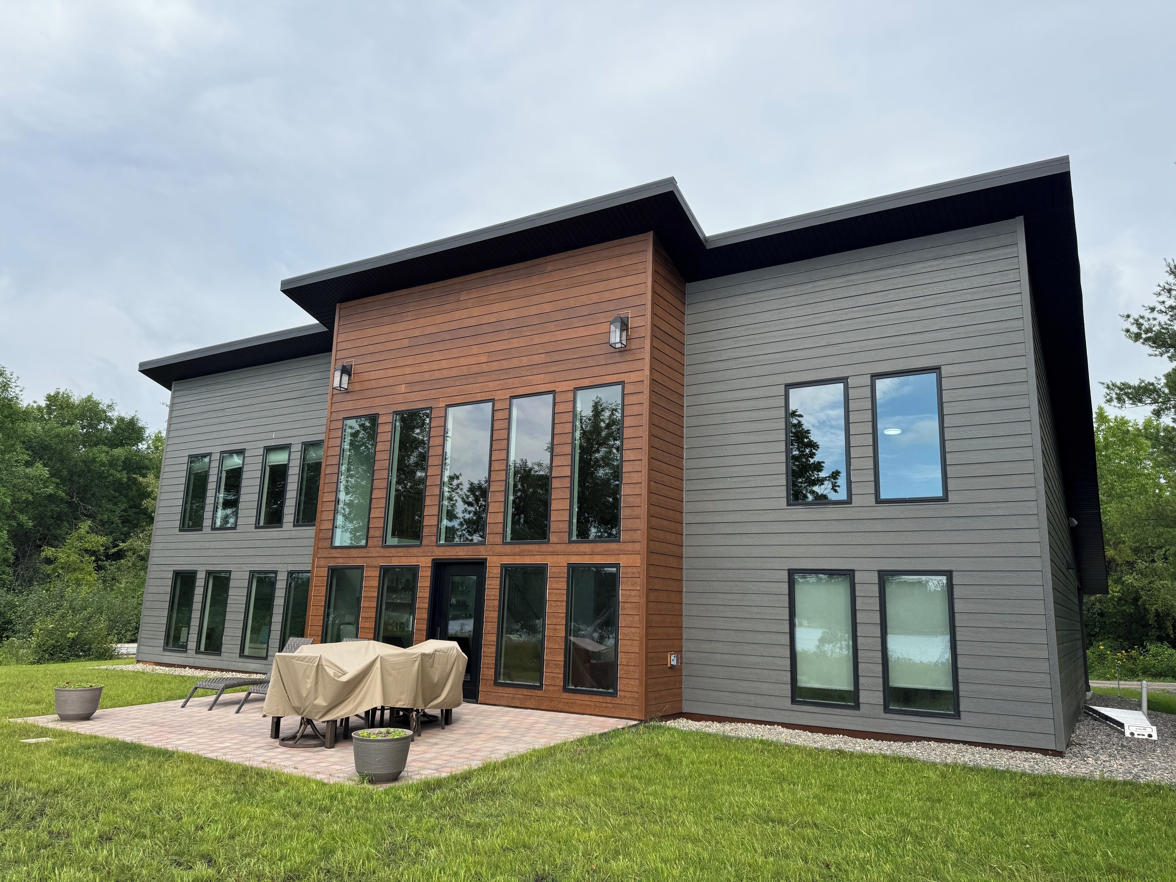 A modern two-story building with large windows and a patio area with outdoor furniture.